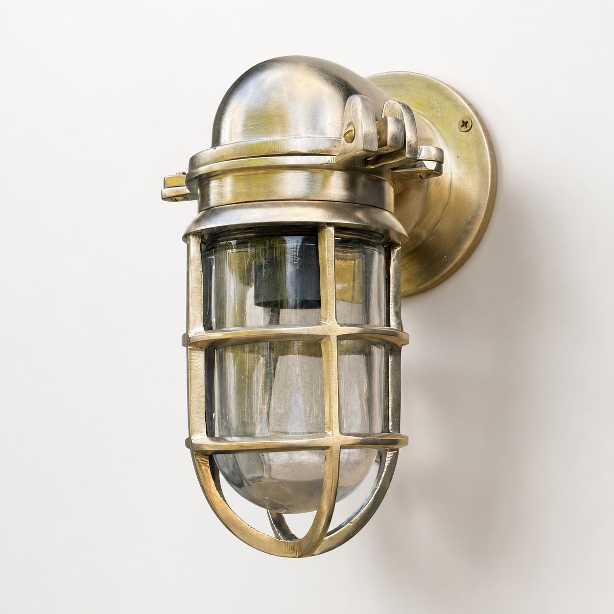 Industrial-style wall sconce with a brushed brass dome top, clear glass shade, and protective metal cage on a plain white background.